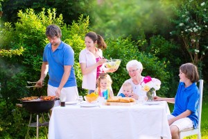 Grill barbecue backyard party. Happy big family - young mother and father with kids teen age son cute toddler daughter and a little baby enjoying BBQ lunch with grandmother eating grilled meat in the garden with salad and bread.